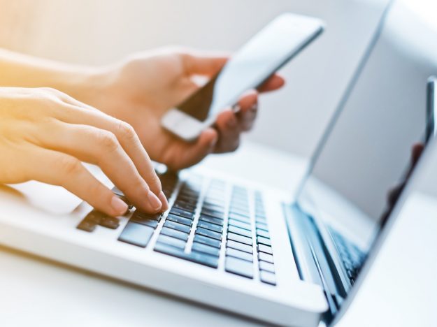 Woman’s hands using laptop and mobile phone at the office